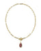 A gold paperclip chain necklace with a toggle clasp and a small oval maroon gemstone pendant, shown on a plain white background.