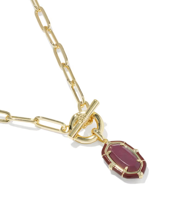 A gold chain necklace featuring a toggle clasp and a dangling oval pendant with a deep burgundy-red stone, shown on a clean white background.