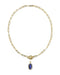 A gold paperclip chain necklace with a toggle clasp and a small oval blue gemstone pendant, shown on a plain white background.