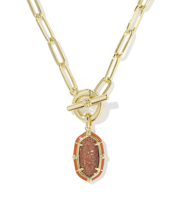 A gold paperclip chain necklace with a toggle clasp and a dangling oval pendant featuring a textured coppery-brown center stone surrounded by a warm orange-red border, shown on a white background.