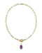 A gold paperclip chain necklace with a toggle clasp and a small oval purple gemstone pendant, shown on a plain white background.
