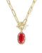 A gold paperclip chain necklace with a toggle clasp and a red oval pendant, shown on a clean white background.