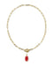 A gold paperclip chain necklace with a toggle clasp and a dangling red oval gemstone pendant, shown on a plain white background.