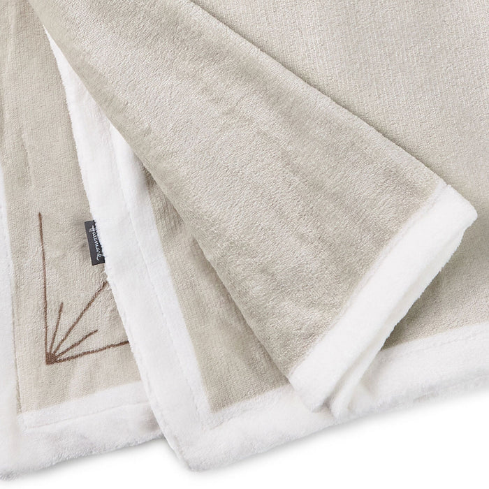 Folded beige blanket with white trim on a light gray background