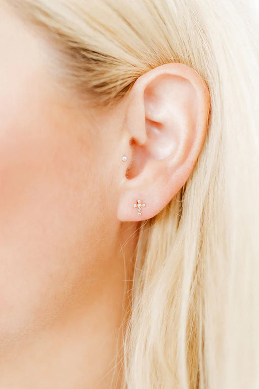 Close-up of an ear with gold stud earrings against a blurred background
