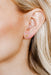 Close-up of an ear wearing a gold earring with a small design.