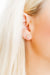 Close-up of an ear wearing a small earring with blonde hair.