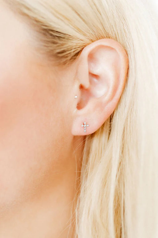 Close-up of an ear with gold stud earrings against a blurred background