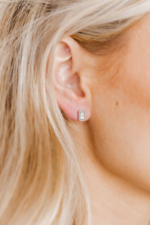 Close-up of a person wearing diamond stud earrings with blonde hair.