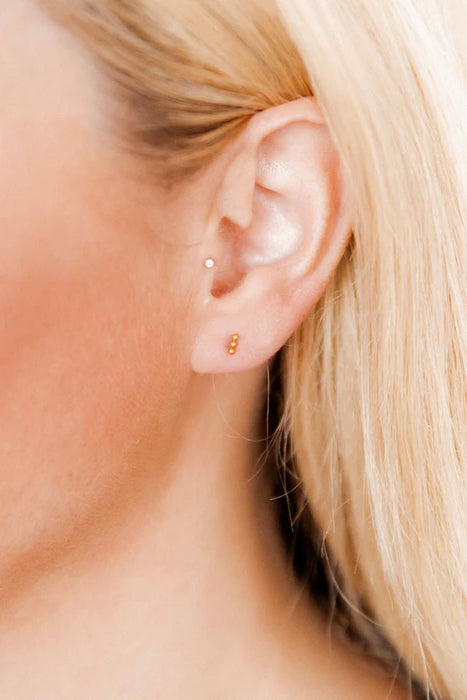 Close-up of a person wearing gold stud earrings with a blurred background
