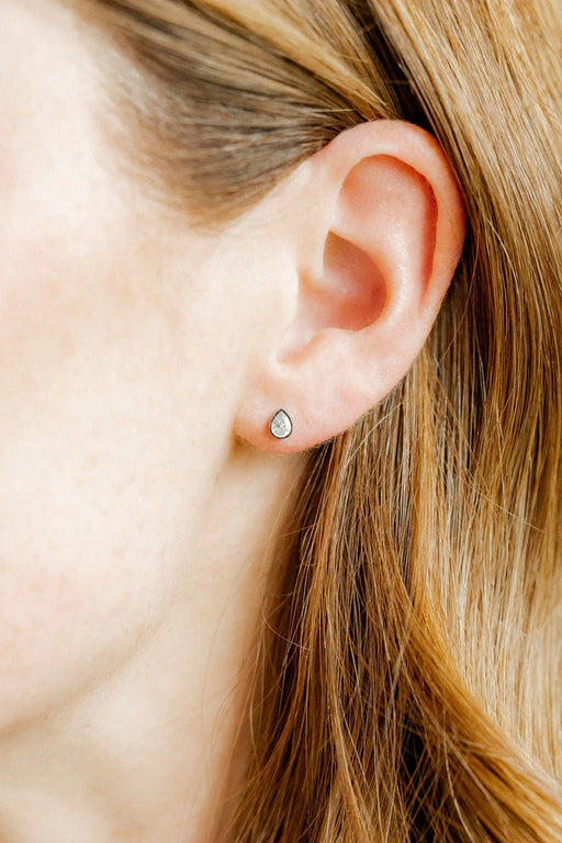 Close-up of an ear with a small earring worn by a person with blonde hair.