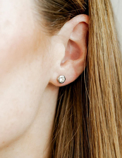Close-up of an ear wearing a small stud earring with blonde hair partially covering the face.