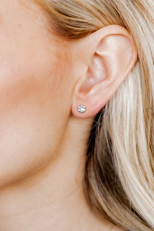 Close-up of an ear wearing a silver earring with a paw print design.
