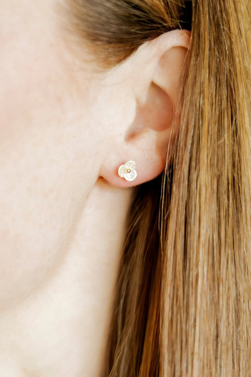 Close-up of an ear wearing a small gold earring with a clear gemstone.