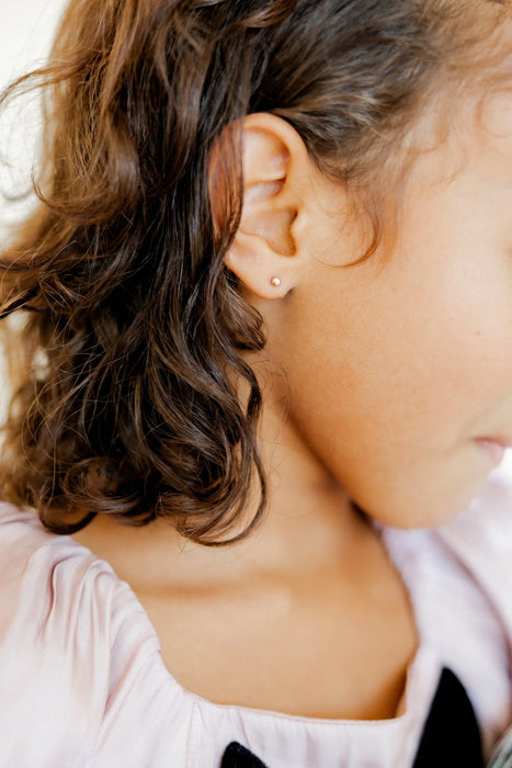 Close-up of a person's ear with an earring, wearing a light pink top.