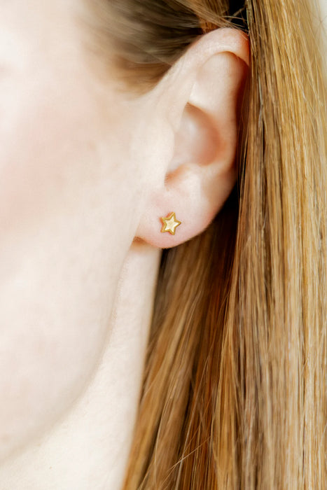 Close-up of an ear wearing a gold star-shaped earring with blonde hair.