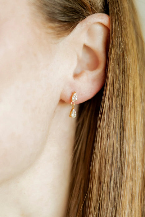 Close-up of an ear wearing a gold earring with a clear gemstone.