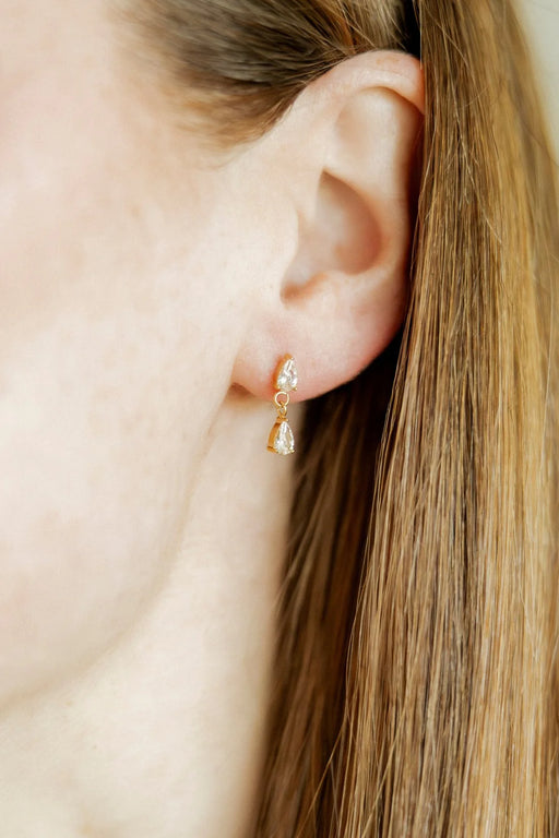 Close-up of an ear wearing a gold earring with a clear gemstone.