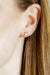 Close-up of an ear wearing a gold stud earring with a blurred background