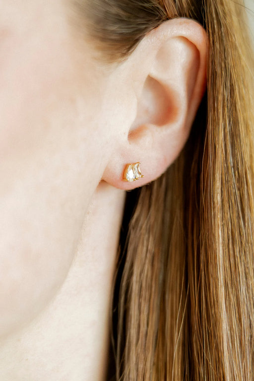 Close-up of an ear wearing a gold stud earring with a blurred background
