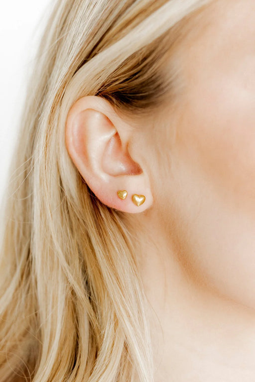 Close-up of an ear wearing gold heart-shaped earrings with a blurred background