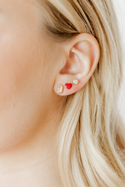 Close-up of an ear wearing two earrings with a heart and a diamond design.