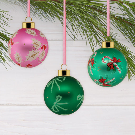 Three colorful Christmas ornaments hanging from a branch on a white wooden background