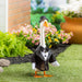 Goose in a tuxedo standing on grass with flowers and a brick wall in the background