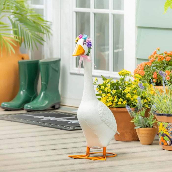 Decorative goose figure with flowers on a wooden deck with potted plants and green boots in the background.