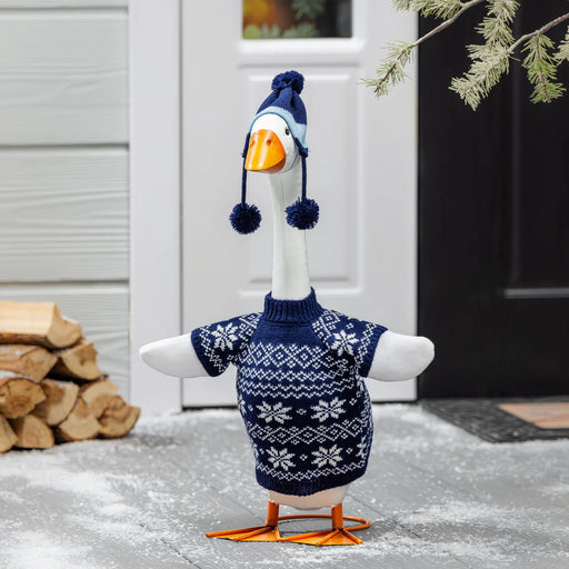 Decorative goose wearing a sweater and hat in front of a house entrance.