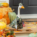 Decorative goose in camouflage outfit with American flag, surrounded by pumpkins and fall leaves.