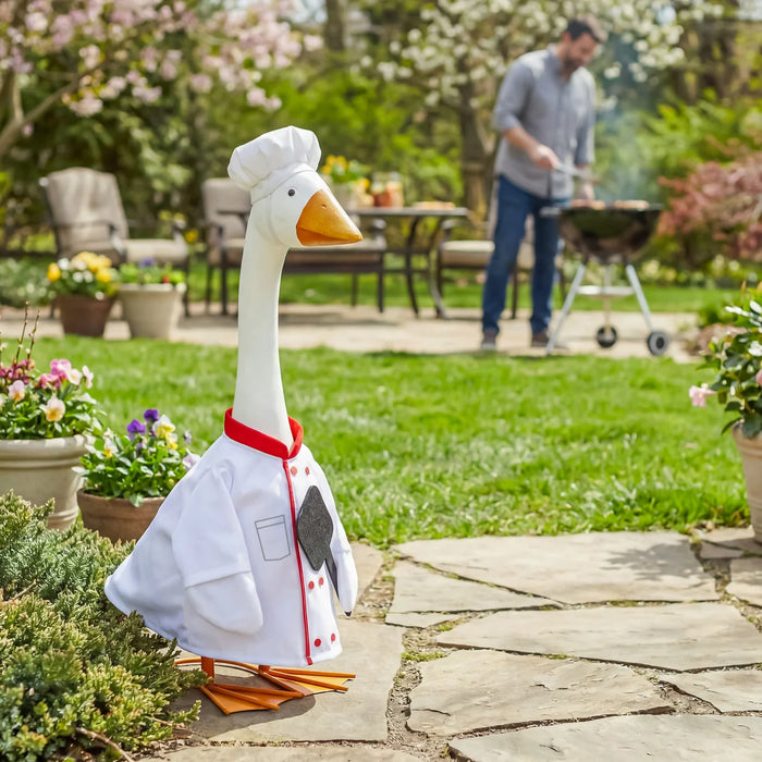 Decorative goose statue in a chef outfit on a stone path with a garden background