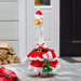 Decorative goose in a Santa outfit standing on a porch with logs stacked against a wall.