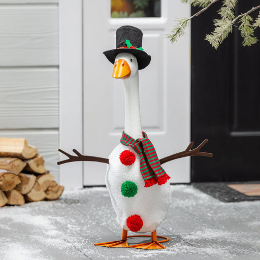 Decorative goose with a top hat, scarf, and pom-poms standing on a snowy ground.