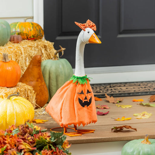 Decorative goose in an orange pumpkin costume standing on a porch with pumpkins and fall leaves.