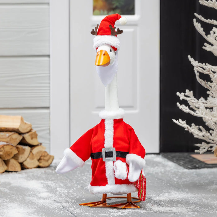 Goose dressed in a Santa Claus outfit with a Christmas tree and logs in the background