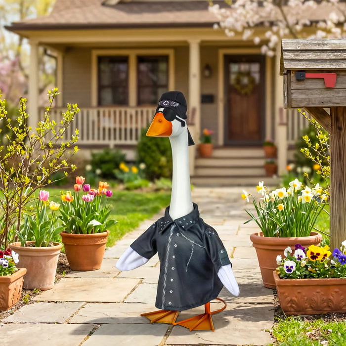 Decorative goose wearing a black jacket in a garden setting with flowers and a house in the background.