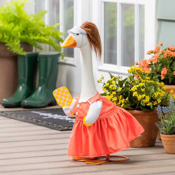 Decorative goose in a pink dress with a checkered paddle on a wooden deck.