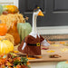 Decorative goose in a pilgrim costume surrounded by pumpkins and autumn leaves.