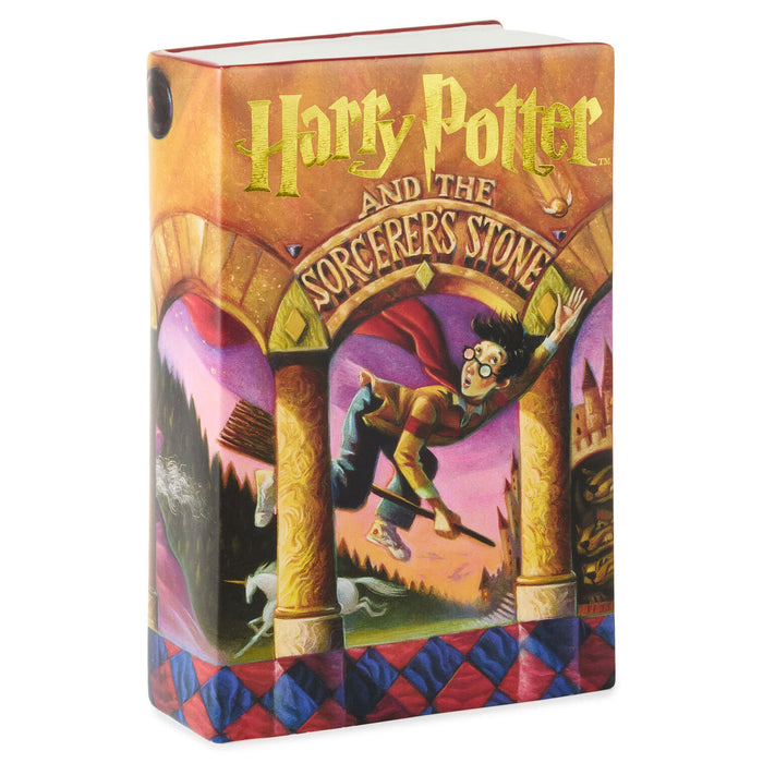A Harry Potter and the Sorcerer's Stone book-themed notebook or journal shown at a three-quarter angle on a plain white background. The cover features the classic illustrated artwork of Harry flying through an archway with castle and magical elements in the background, and the title 'Harry Potter and the Sorcerer's Stone' in large gold lettering at the top.