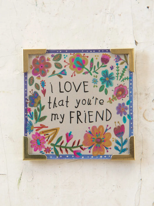 Decorative sign with floral design and text 'I love that you're my friend' on a light background