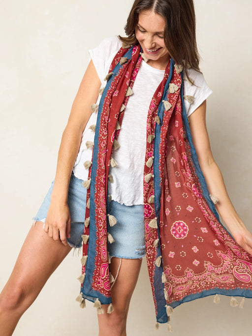 Woman wearing a patterned scarf with pom-poms against a plain background