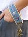 Hand wearing a blue embroidered wristlet with a keychain on a white background