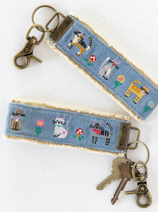 Keychain with embroidered cat designs on a blue fabric strap.
