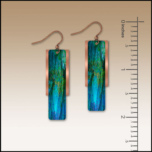 Pair of blue and green earrings with a ruler for scale on a beige background