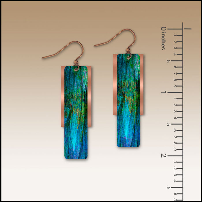 Pair of blue and green earrings with a ruler for scale on a beige background