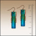 Pair of blue and green earrings with a ruler for scale on a beige background