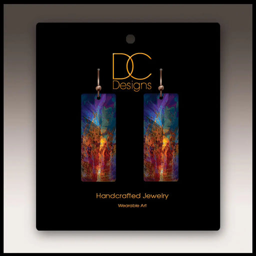 Colorful earrings on a black card with 'DC Designs' branding