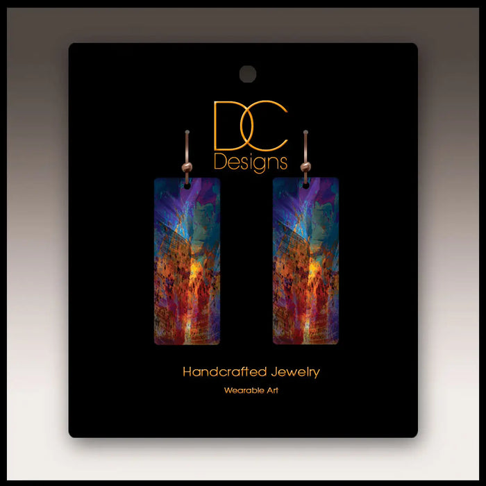 Colorful earrings on a black card with 'DC Designs' branding