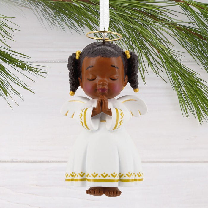 Angel figurine ornament with braided hair and a white outfit with gold patterns, hanging from a branch.